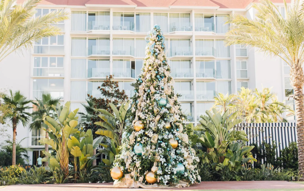 Decorated Christmas tree in front of a building with palm trees on a sunny day.