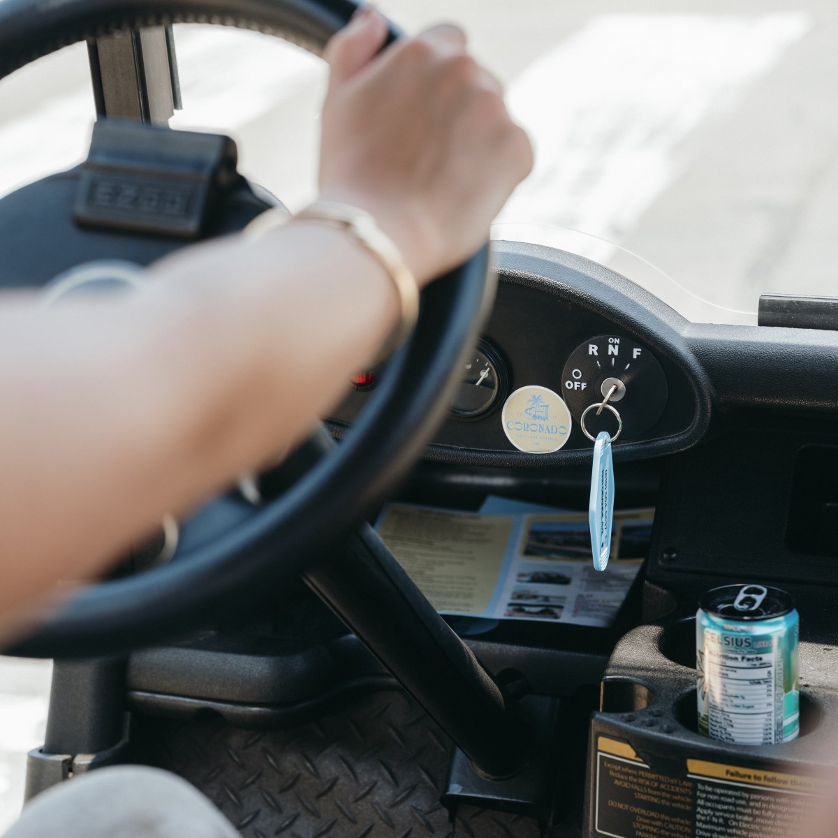 Person driving, holding steering wheel, with dangling mask and drink can.